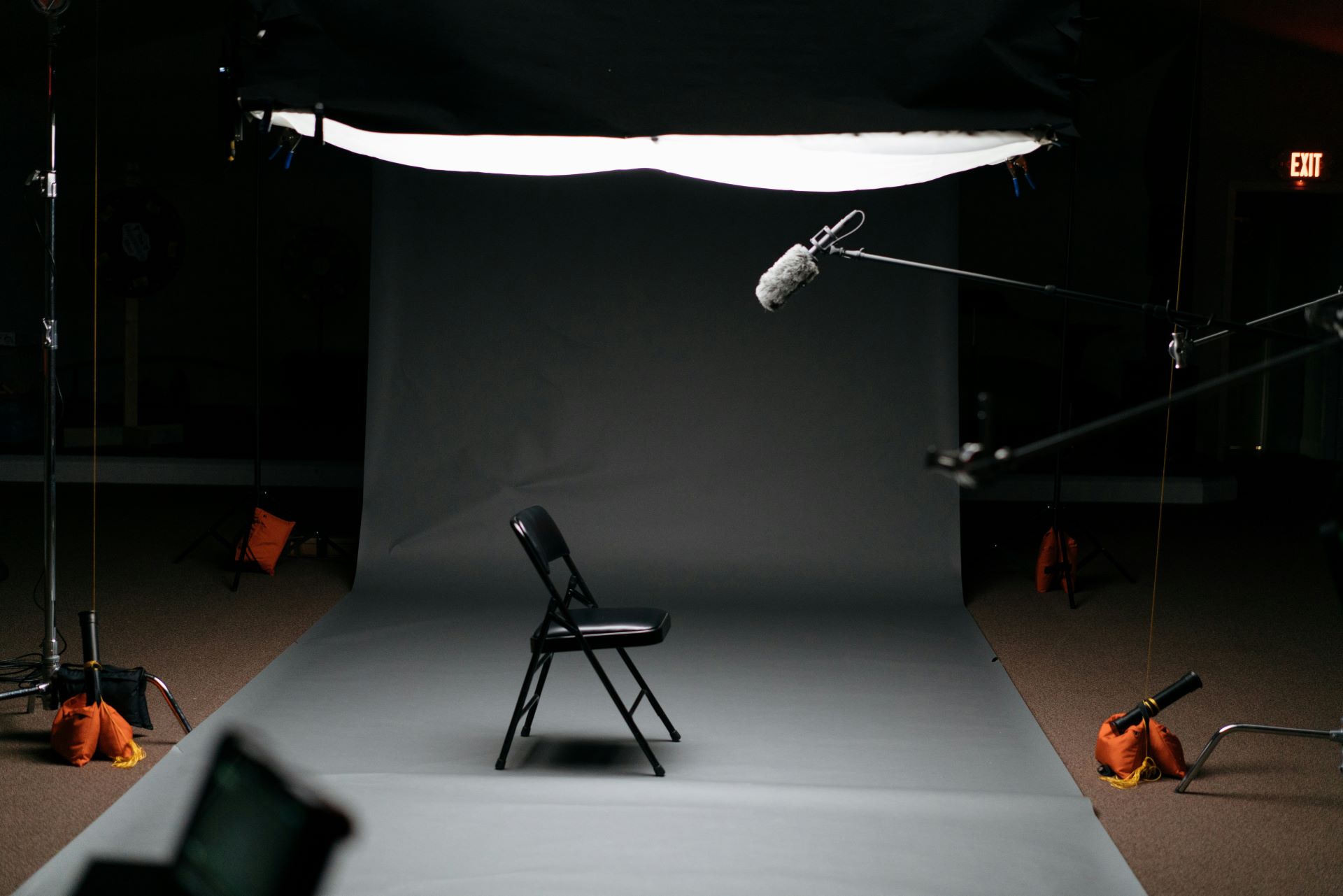 A fold up chair in the centre of a studio with a boom microphone pointing down from above
