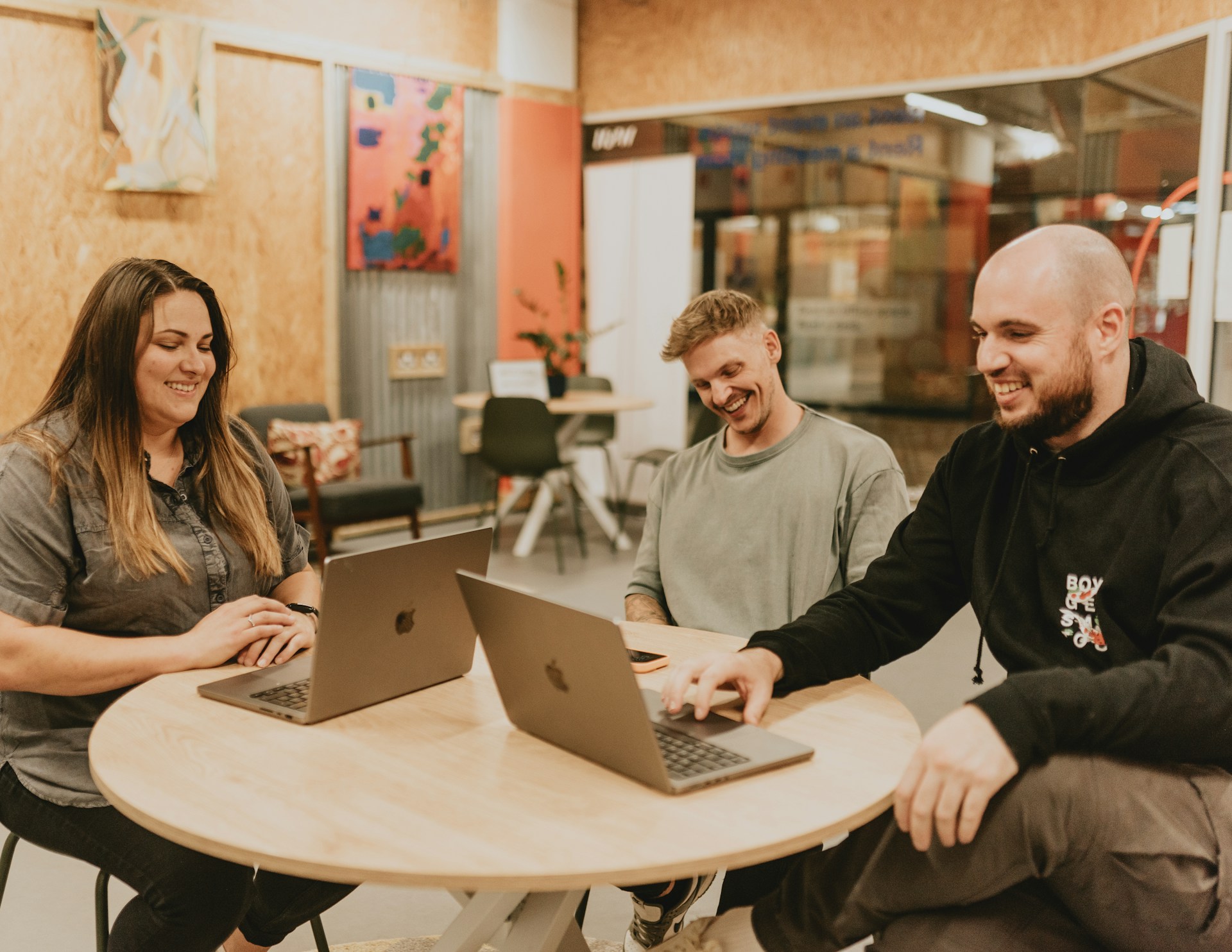 Three people sit around a table with laptops