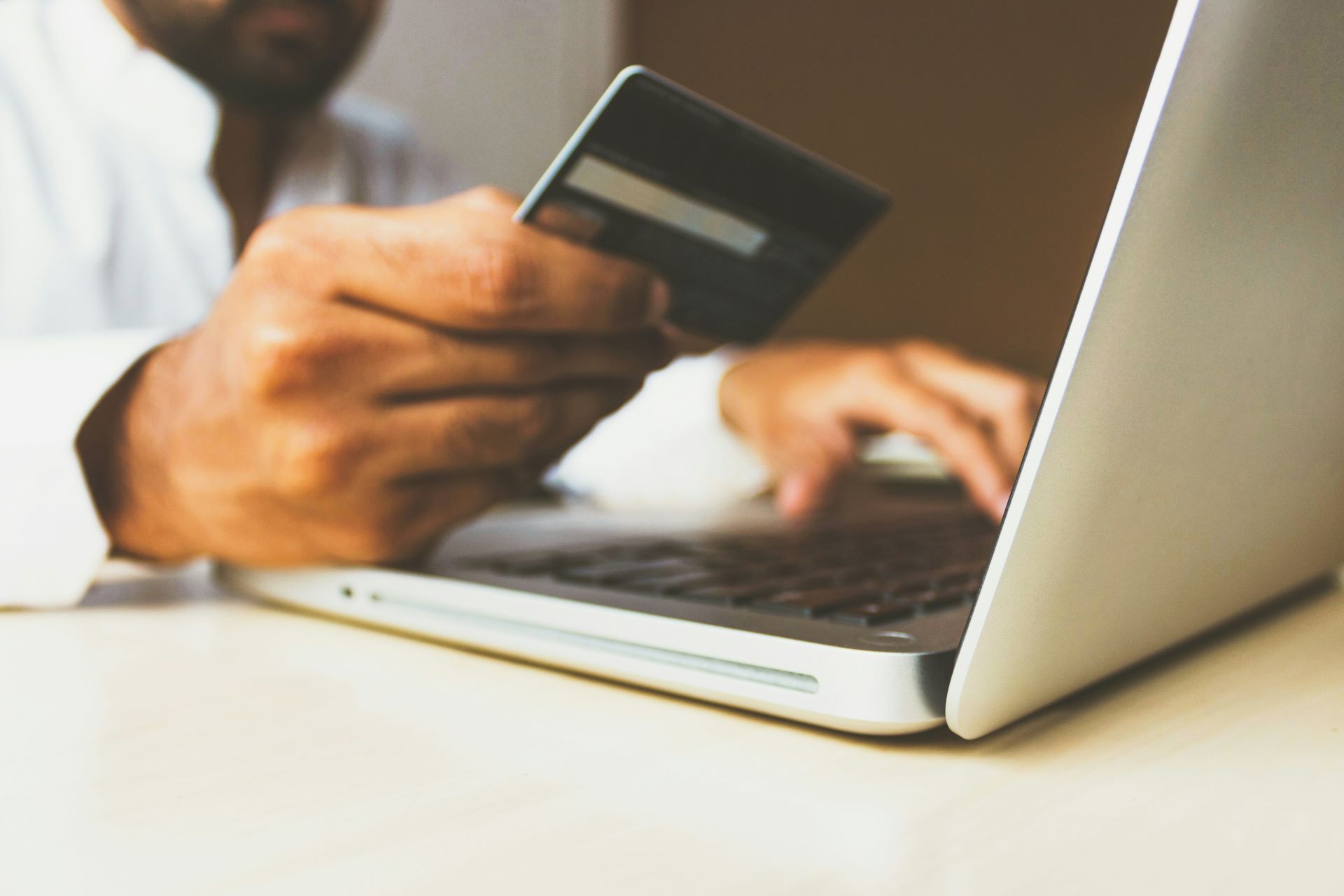 Close up of a person holding a credit card while typing on a laptop