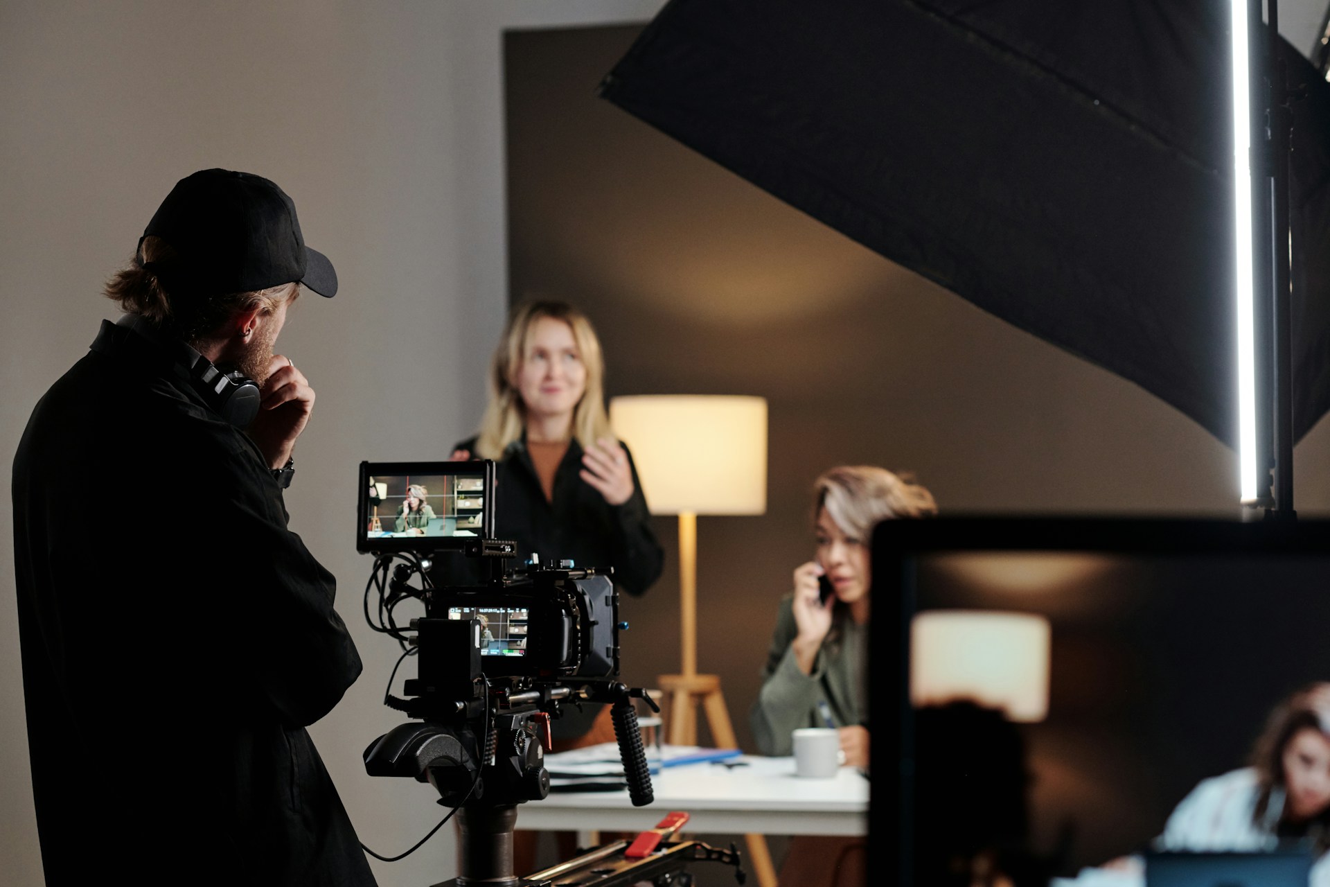 A camera operator stands by a camera. Two actors can be seen on set