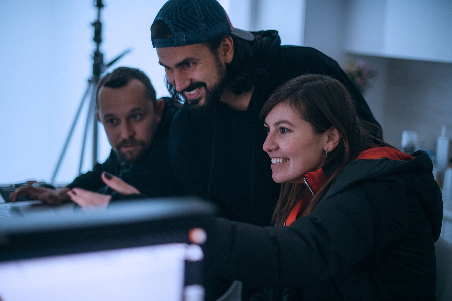 Two men and one woman smile as they watch a screen at a desk