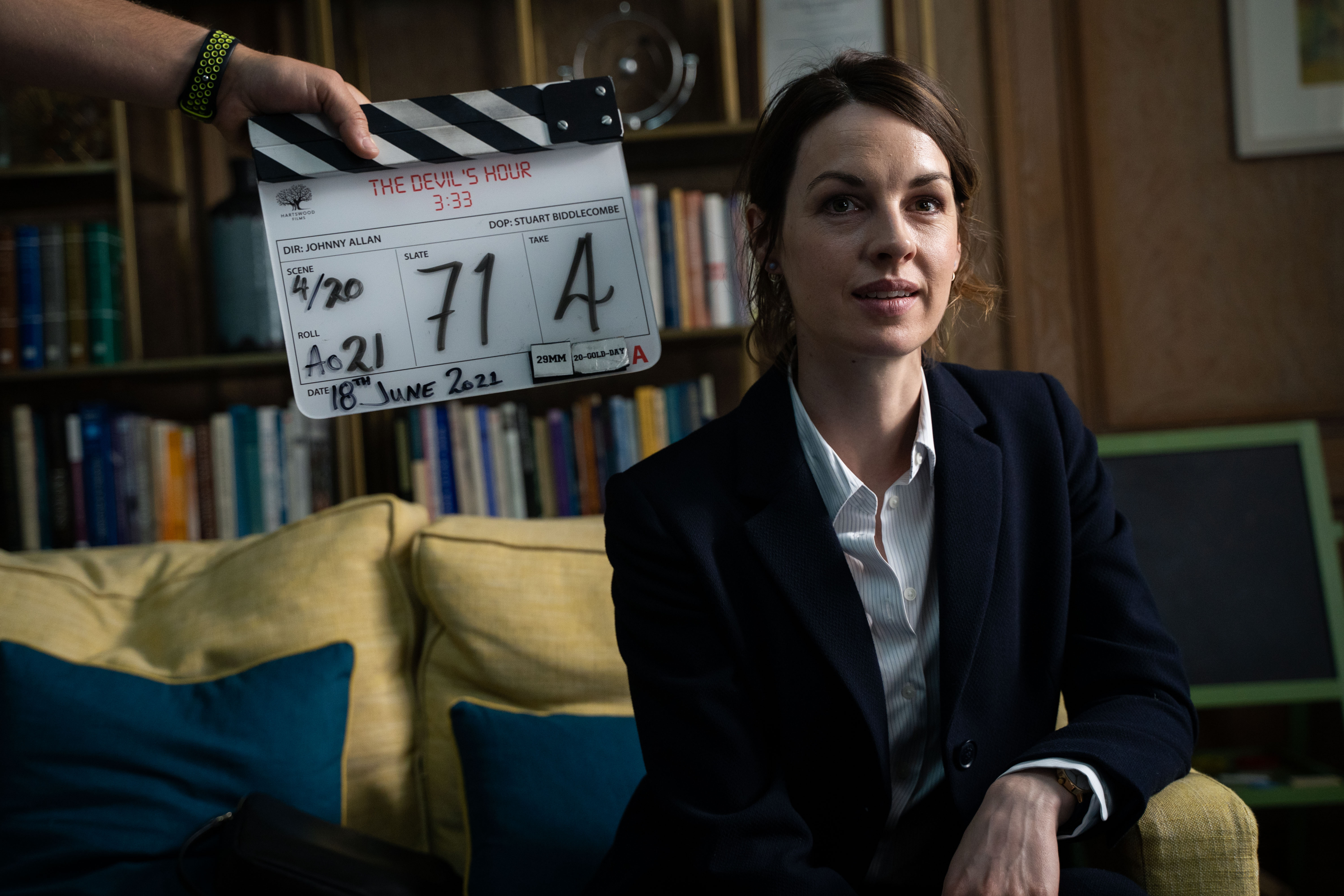 Jessica Raine on set of The Devil's Hour seated on a yellow sofa behind a clapper board