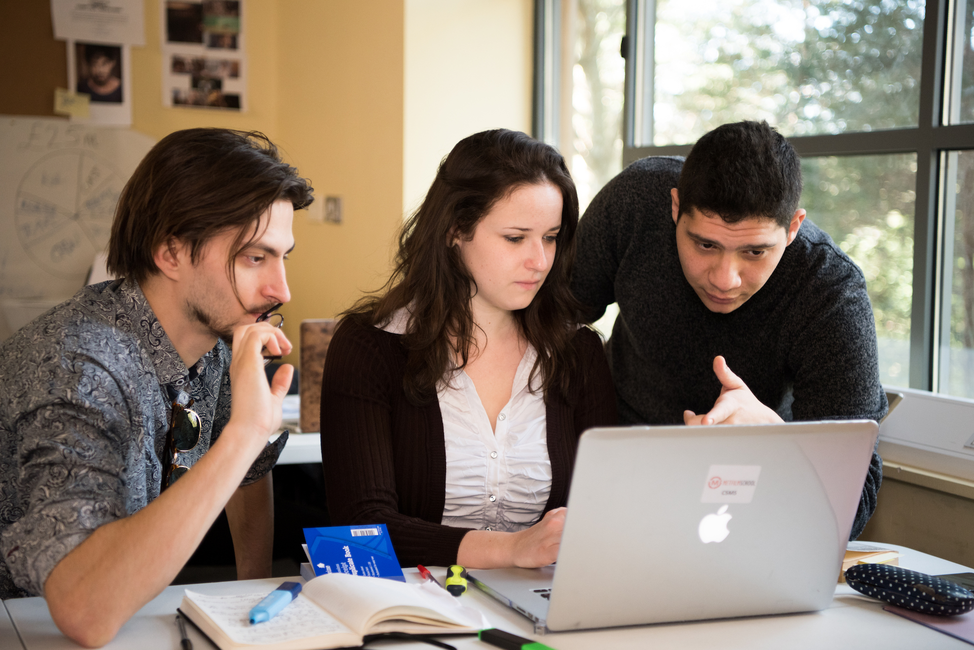 Three young people gathered around a laptop on a desk