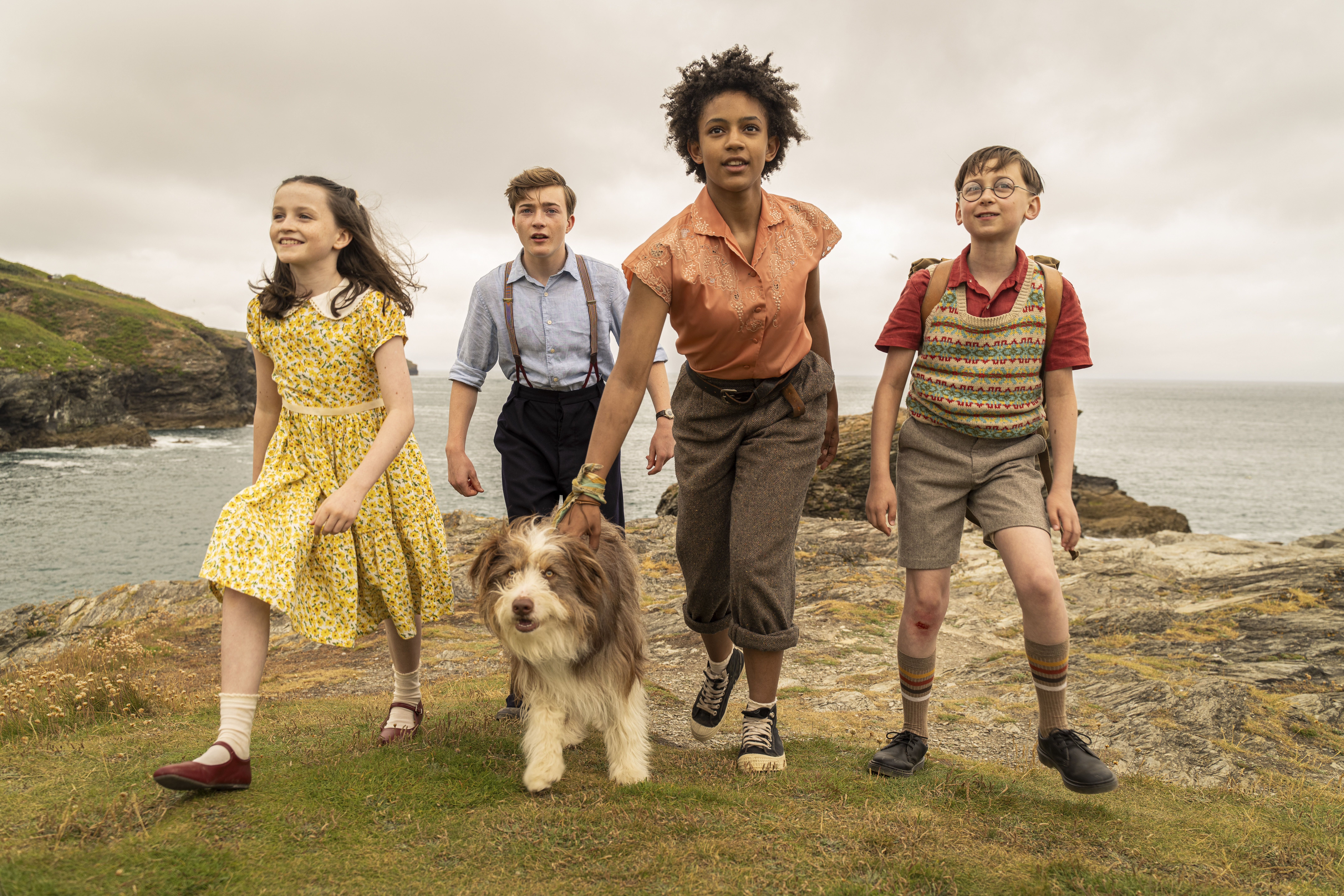 Still of young cast of The Famous Five walking toward the camera away from a cliff edge