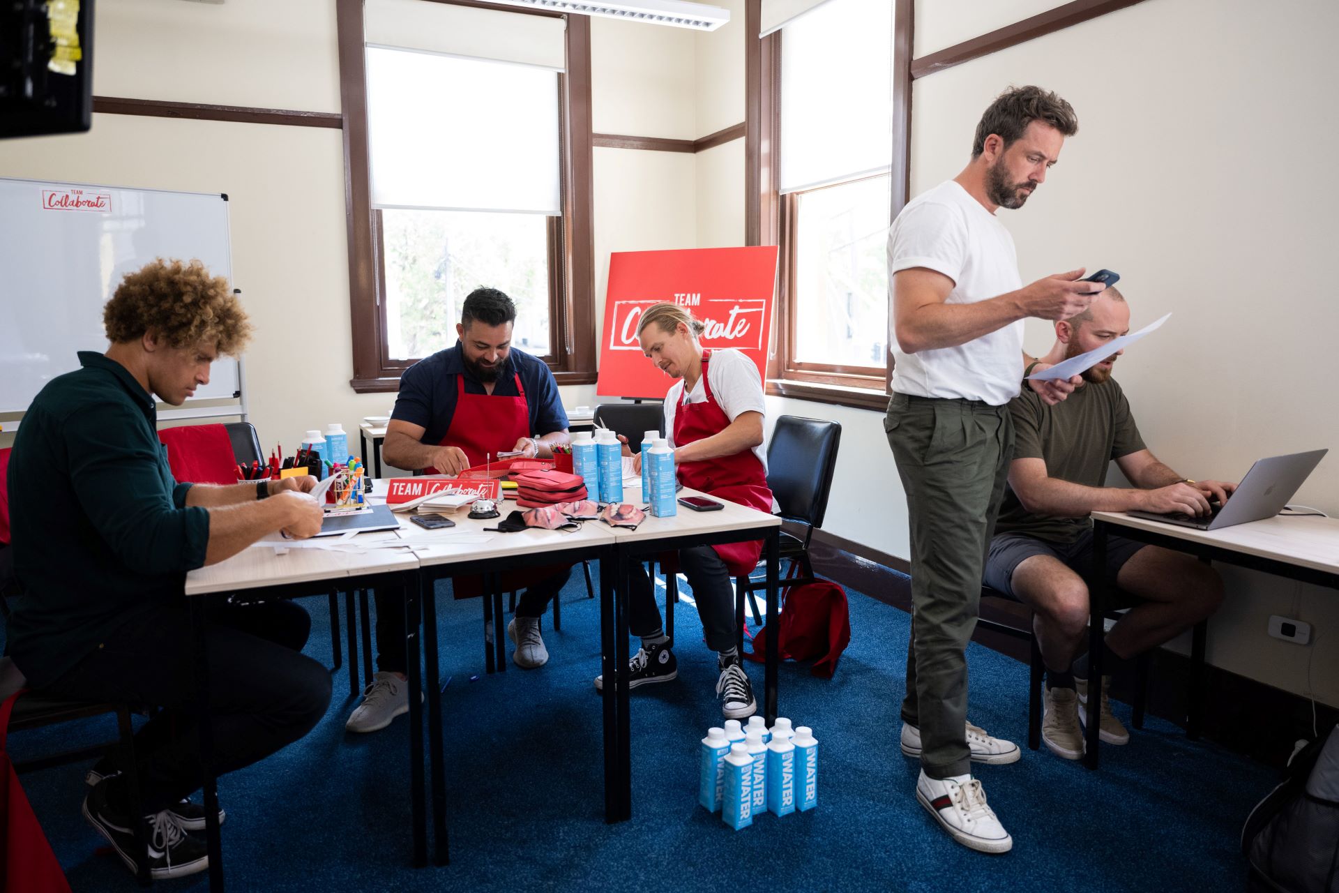 Several people sit around tables in a room working on a project