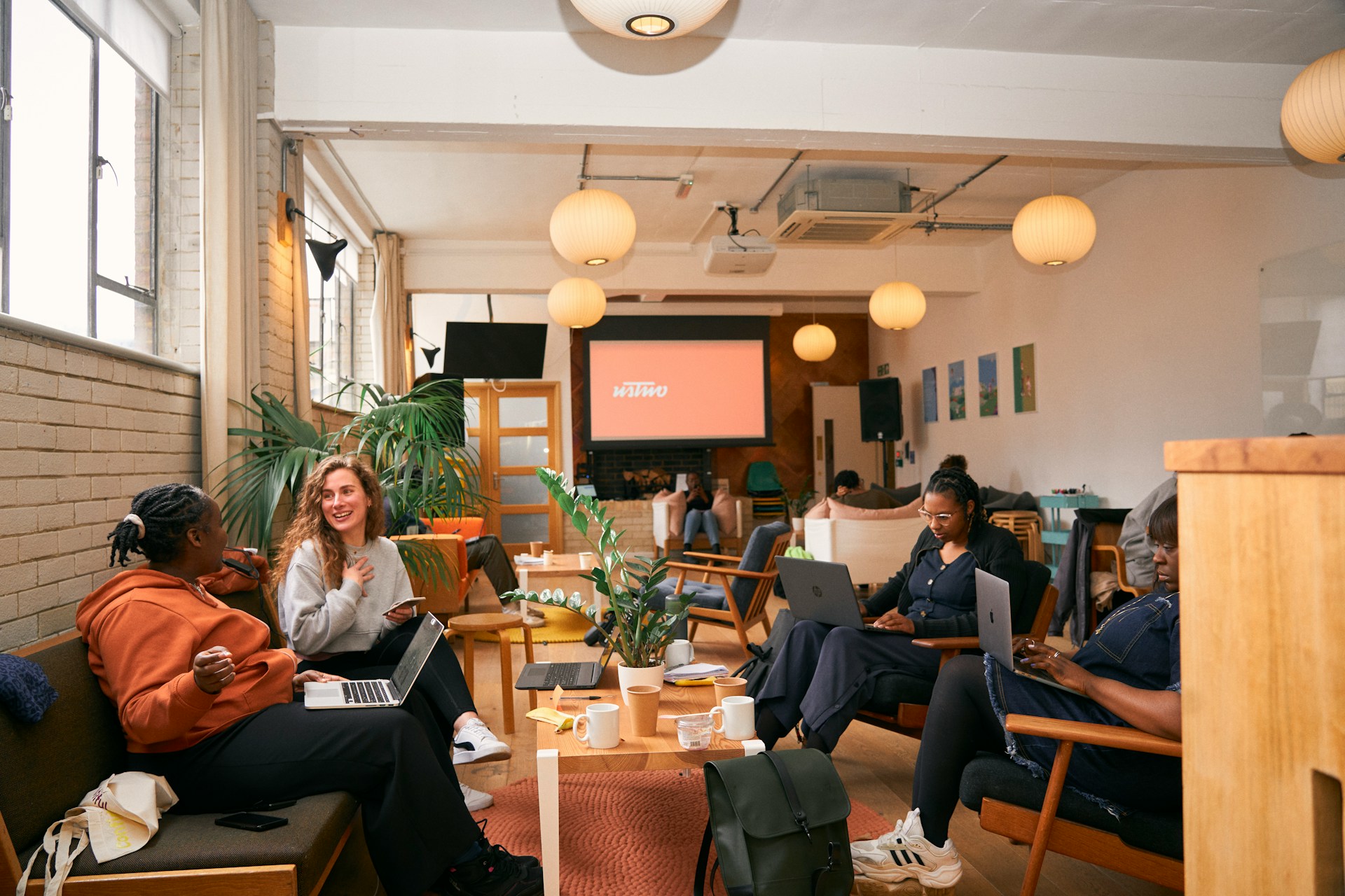 A group of people sit around a table in a cafe working on laptops