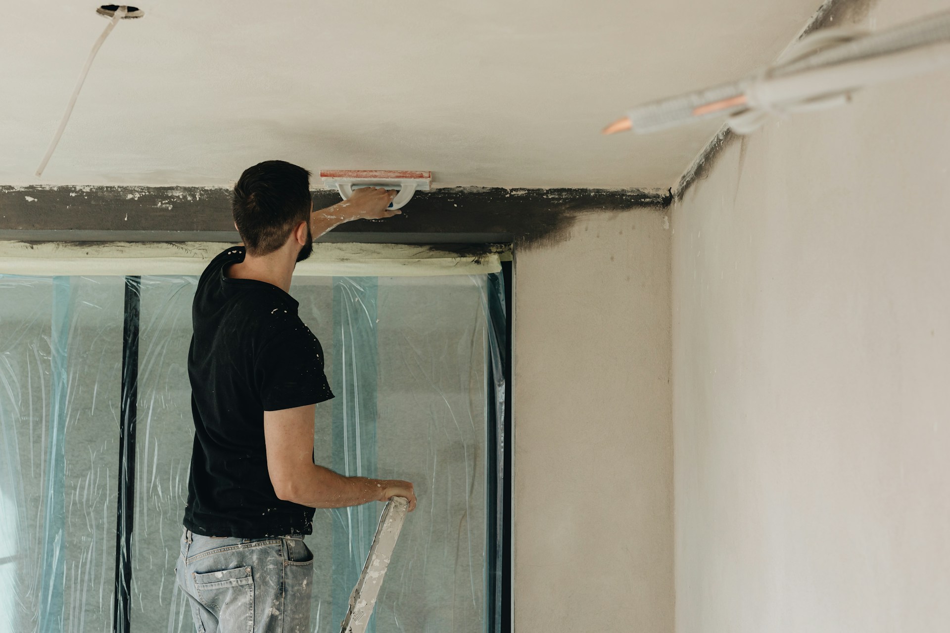 A man stands on a ladder plastering a ceiling
