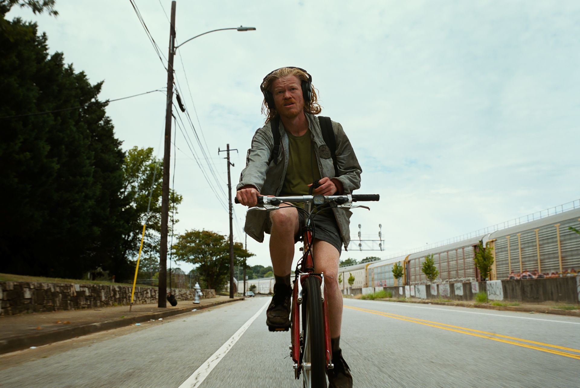 A man wearing headphones and a backpack rides a bicycle in the middle of an empty road.