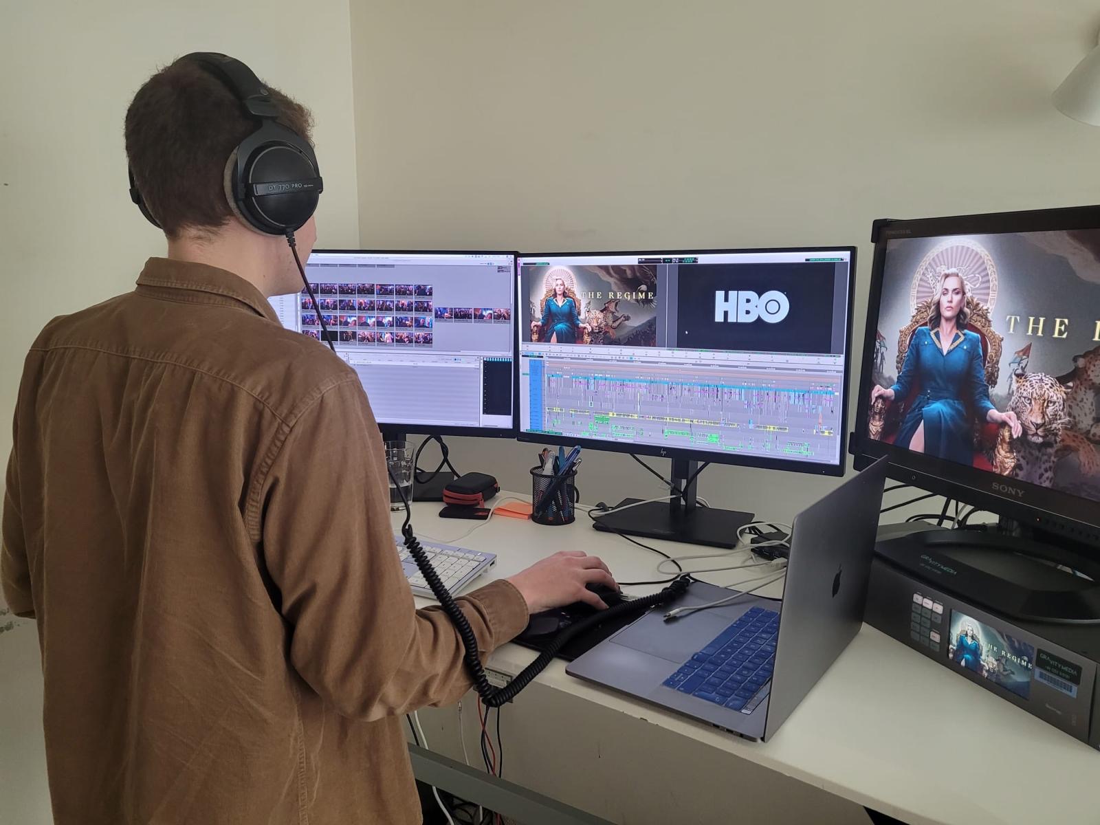 A person facing a set of computer monitors edits a sequence from a drama called The Regime.