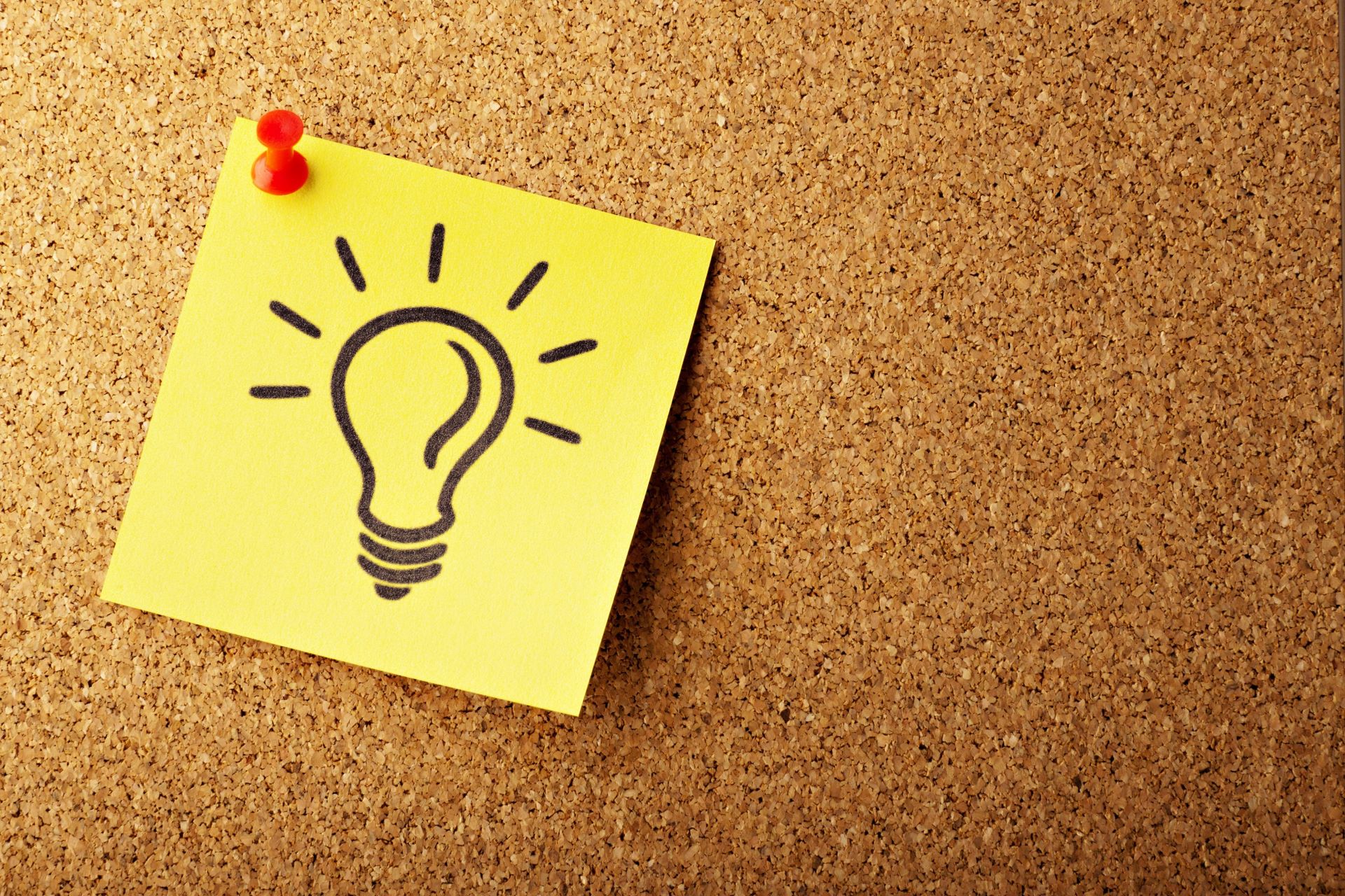 A Post-It note with a drawing of a lightbulb pinned to a cork board